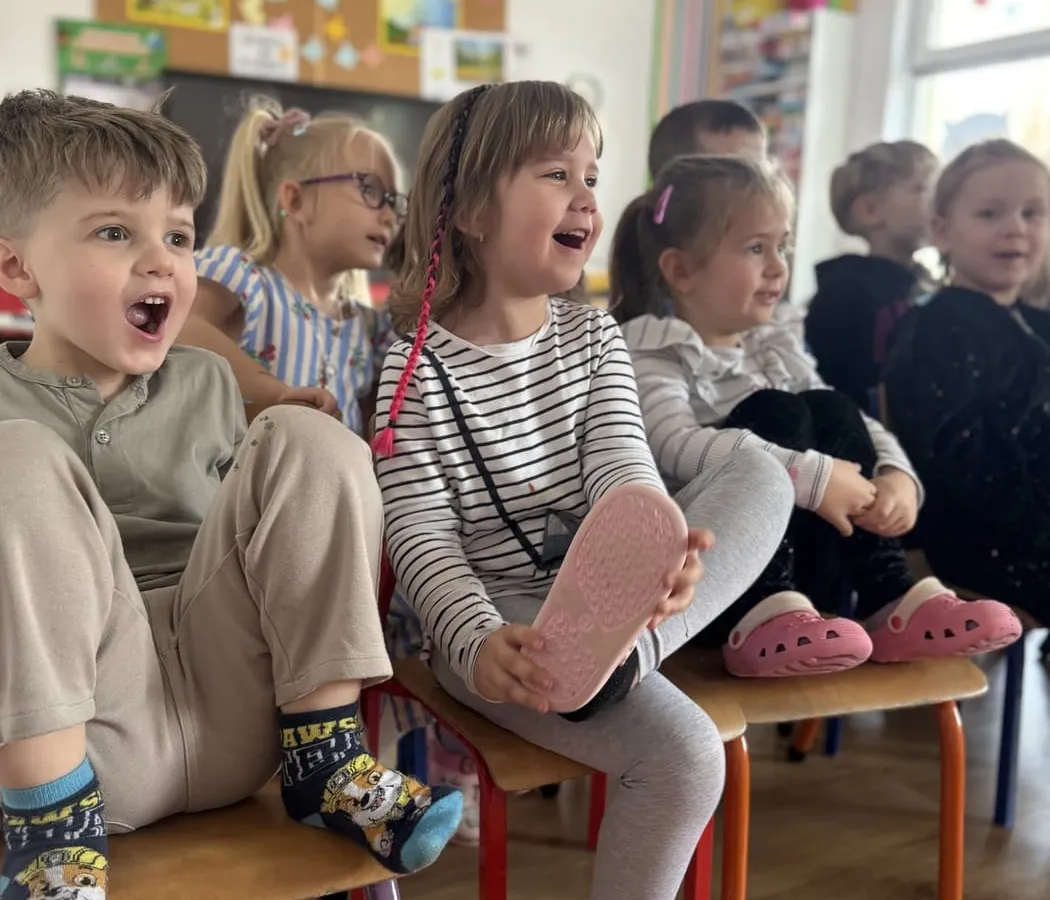 Roześmiane dzieci na ławeczce w sali przedszkola Wesołe Sowy