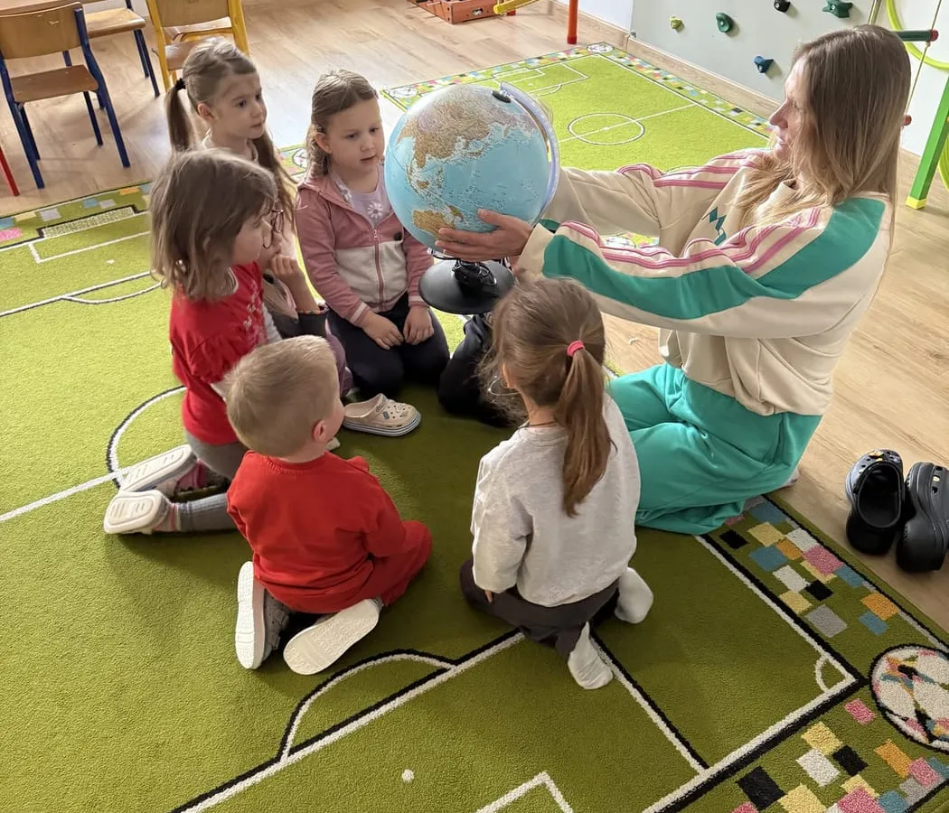 Zajęcia w sali przedszkola Wesołe Sowy — dzieci na dywanie poznają globus